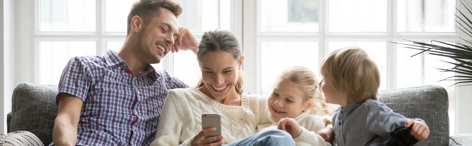 family of four setting on couch looking at smartphone screen