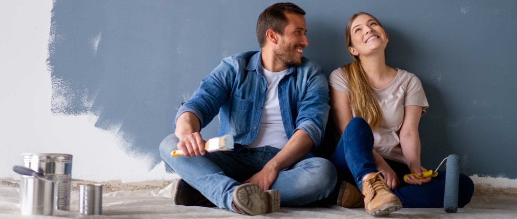 Man, and women sitting on floor next to paint cans painting room blue