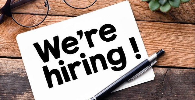 we're hiring sign laying on wood table