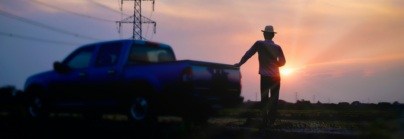 man standing at back of pickup watching sunset with powerlines in background