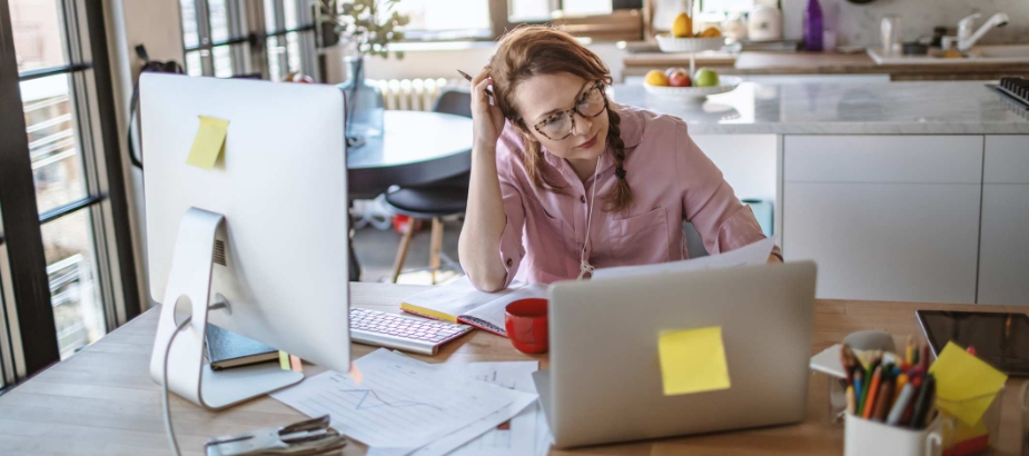 Women sitting in front of laptop and computer at desk covered in bills and notes