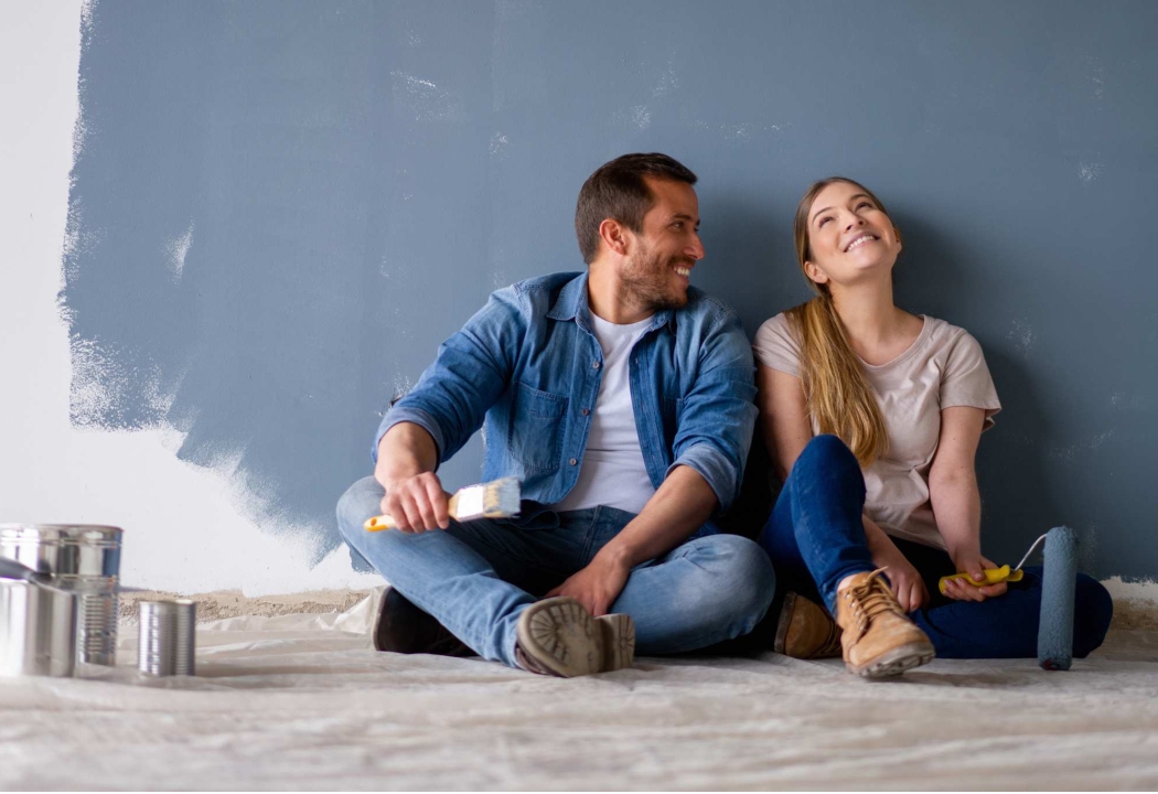 Man, and women sitting on floor next to paint cans painting room blue