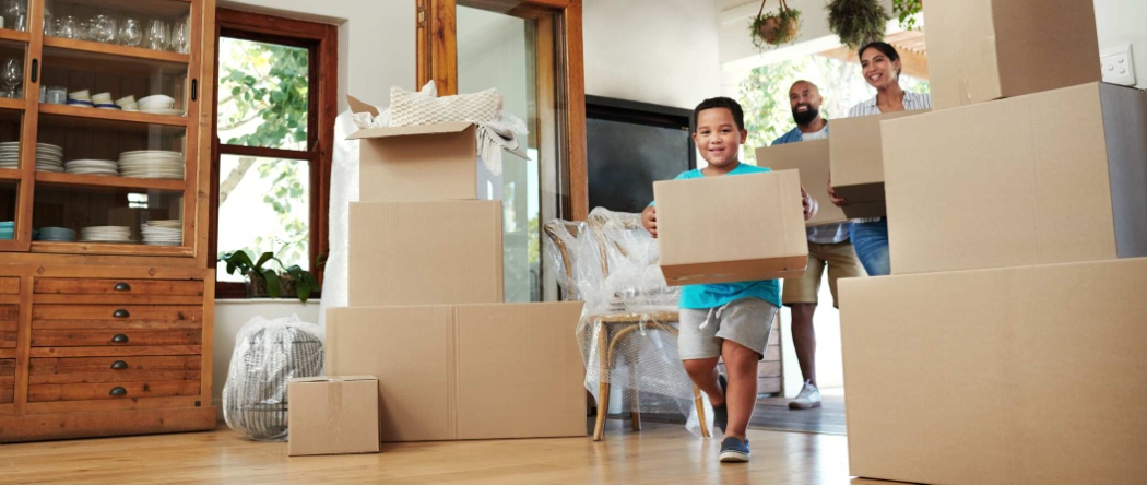 Young family with son carrying boxes into new home.