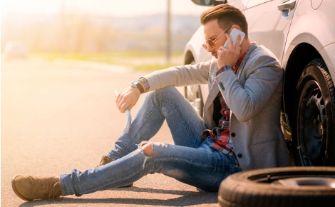 Man sitting next to his broken down car on the phone.