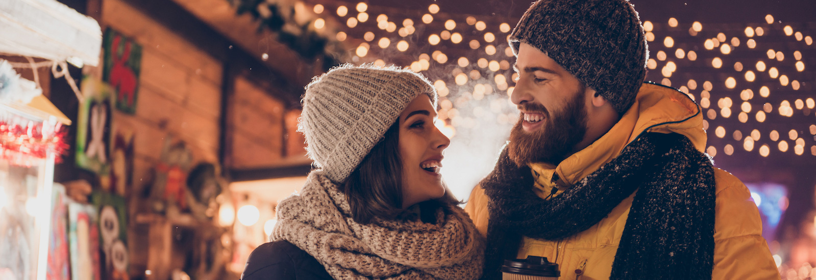 man and women in stocking caps and scarves walking under holiday lights