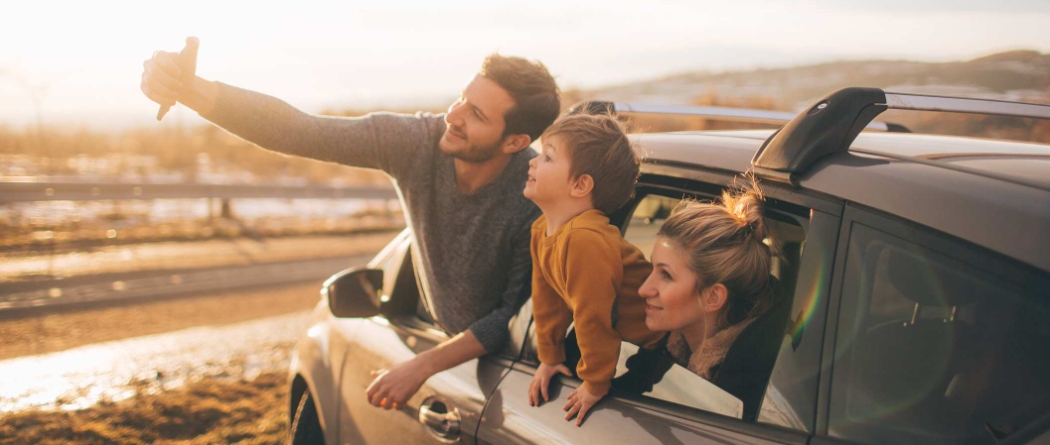 Father, mother and child hanging out of car window taking a selfie picture with phone