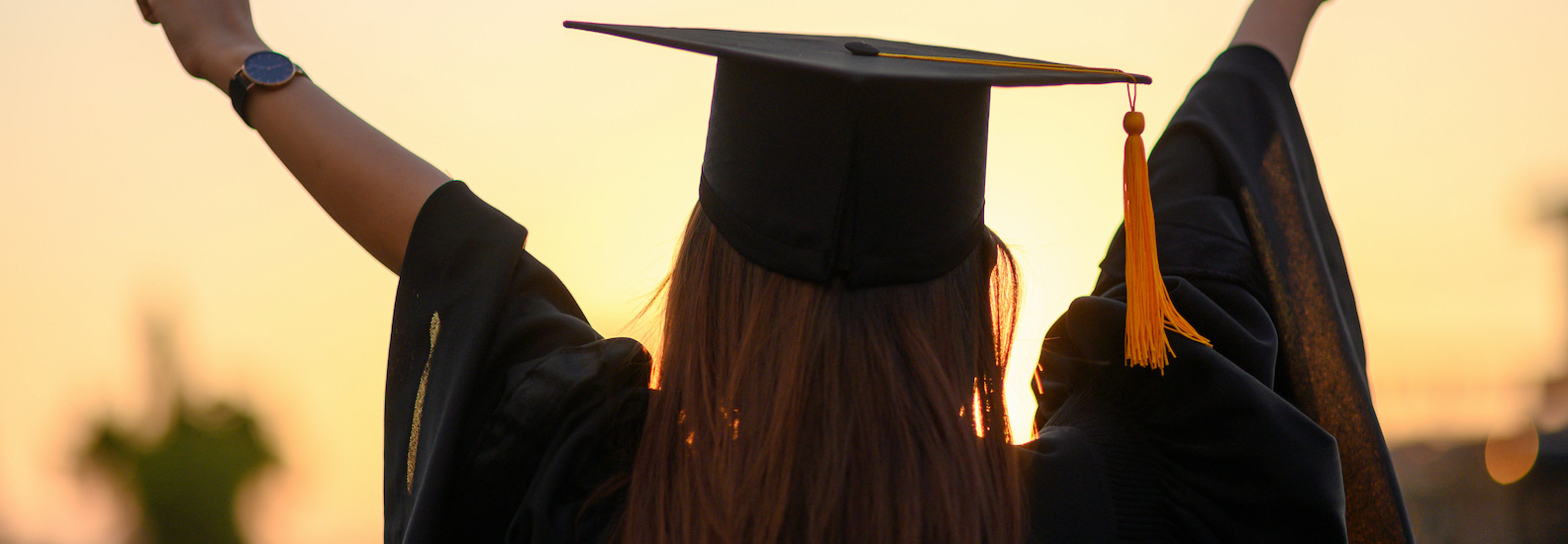 woman wearing black graduation hat and gown with arms up celebrating