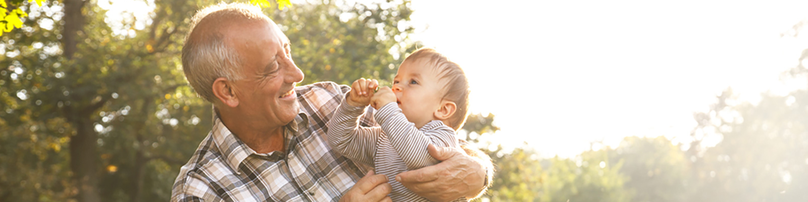 elderly man happily holding a baby outdoors